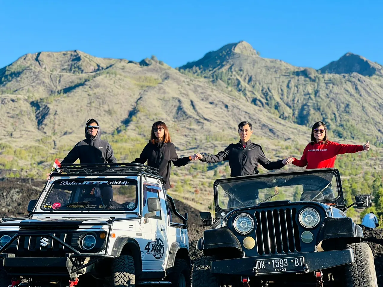 Two jeeps parked on volcanic ground with four guests standing in the open roofs