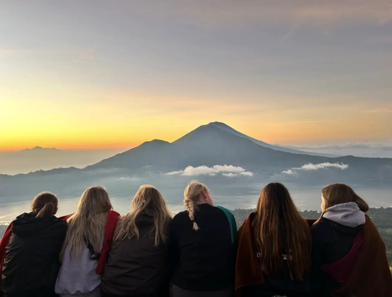 Five guests sitting side by side watching the sunrise over a volcano