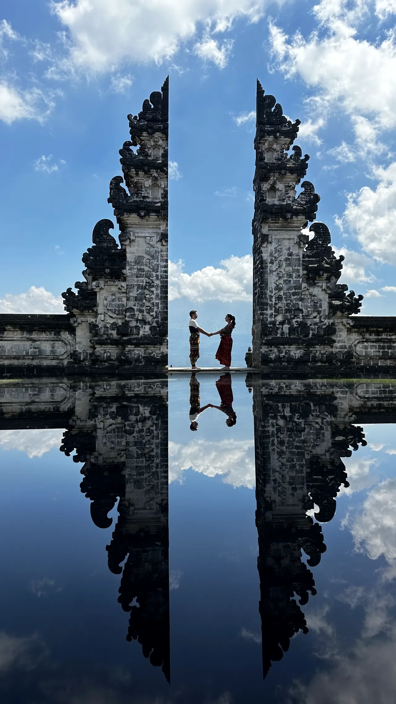 A couple holding hands between the split gate at Lempuyang, mirrored in water