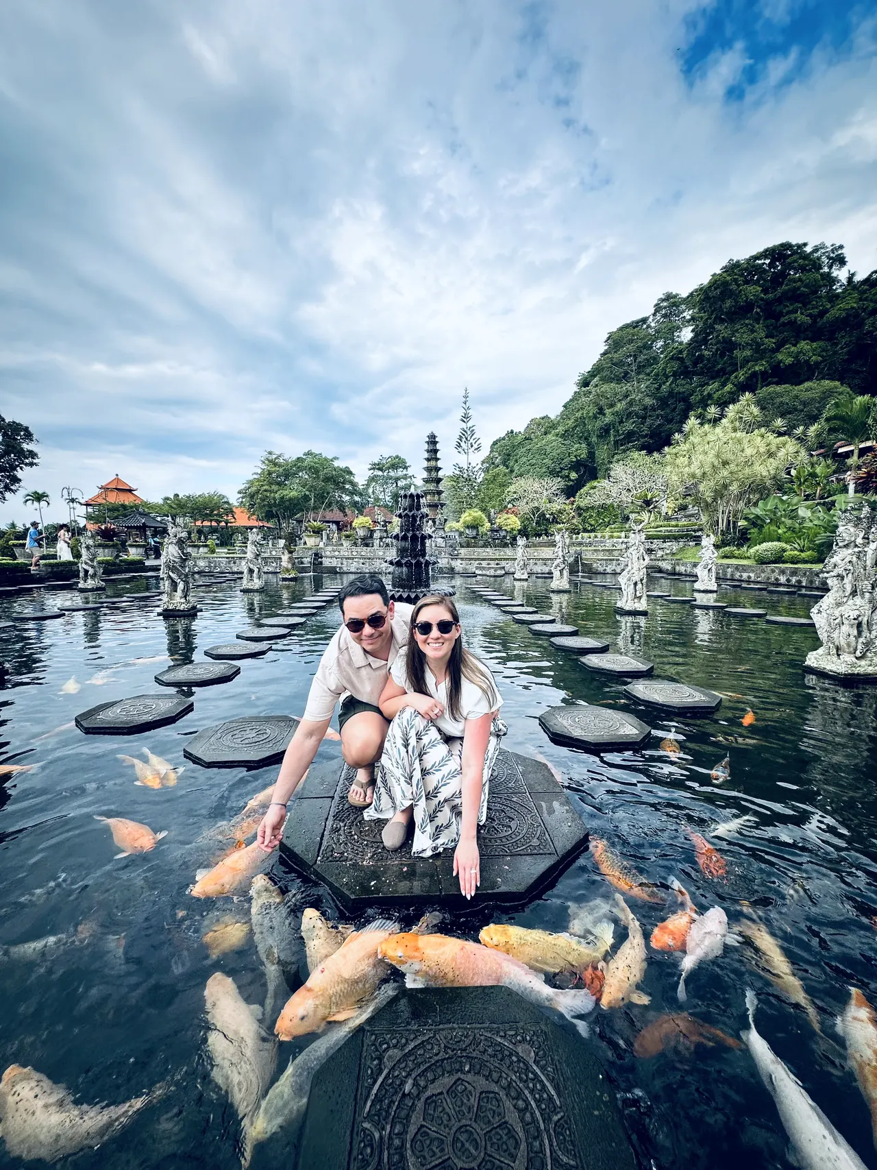 Two visitors crouched on stepping stones among koi at Tirta Gangga